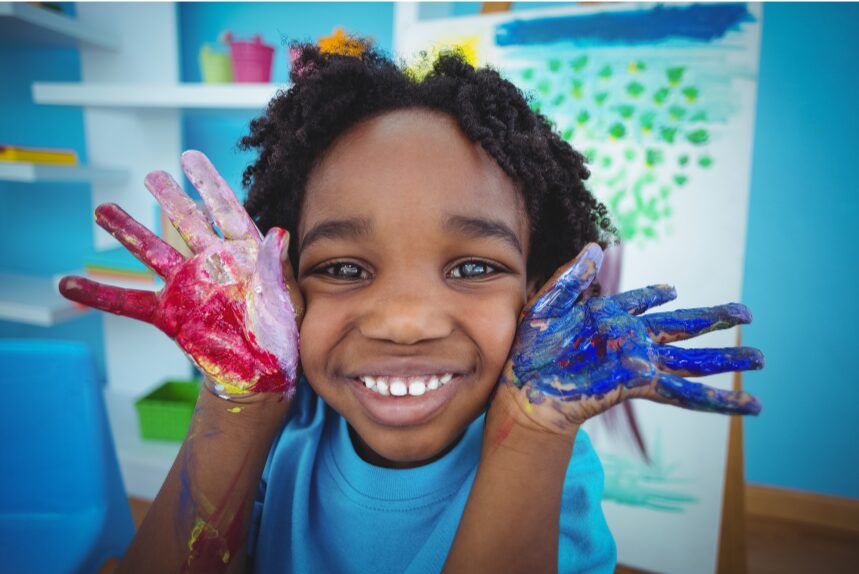 Photo of a smiling child with hands covered in paint